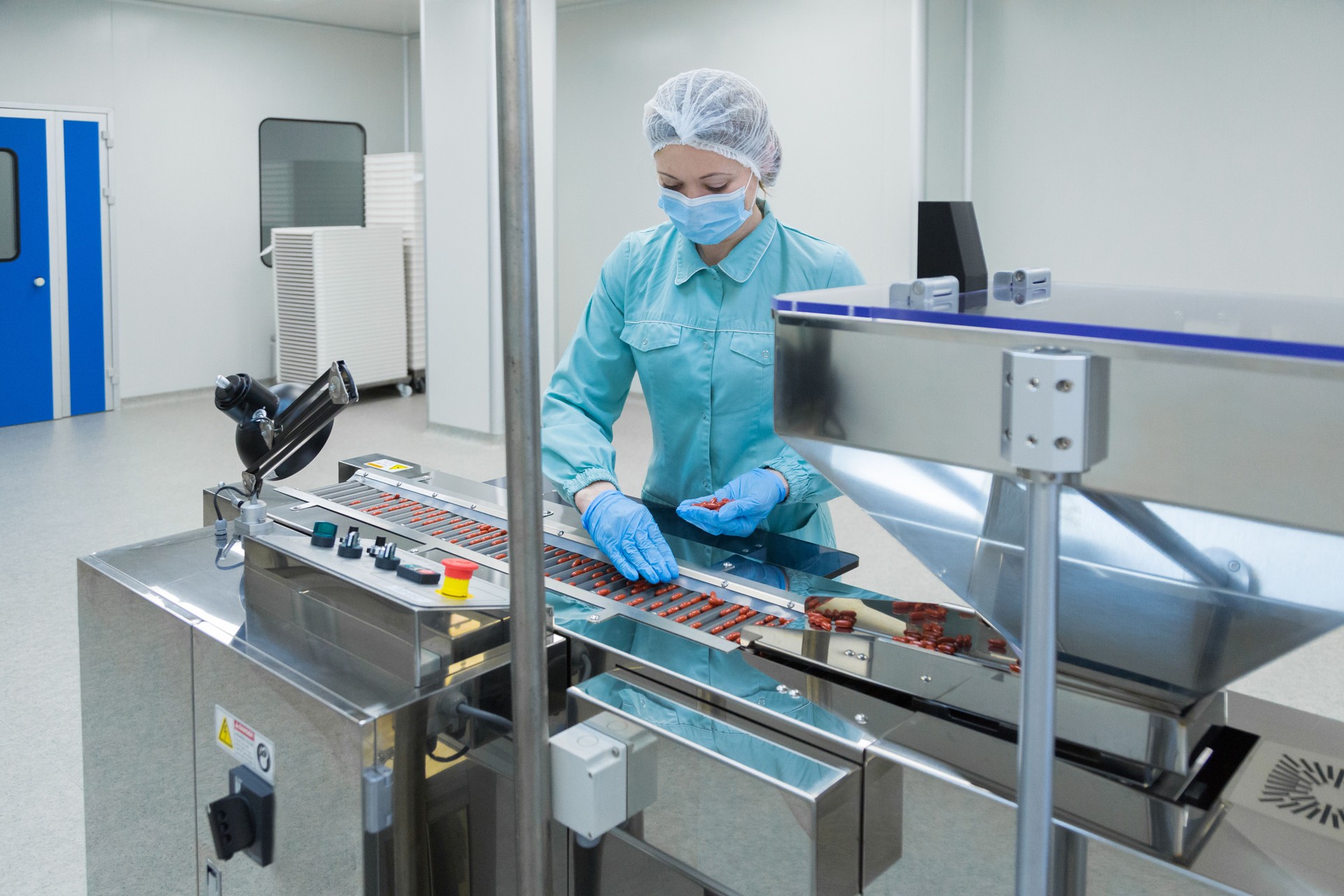 Pharmacy industry woman worker in protective clothing operating production of tablets in sterile working conditions